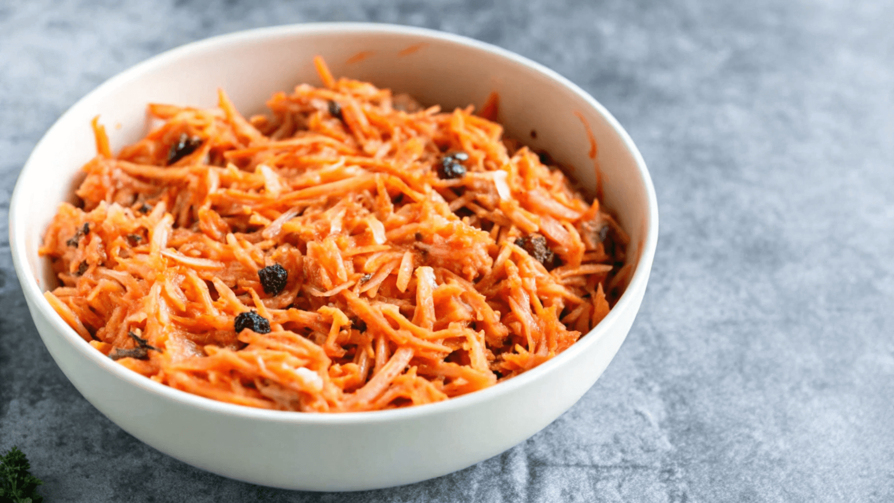 Carrot and raisin salad in a white bowl with grated carrots, raisins, nuts, and a creamy dressing.